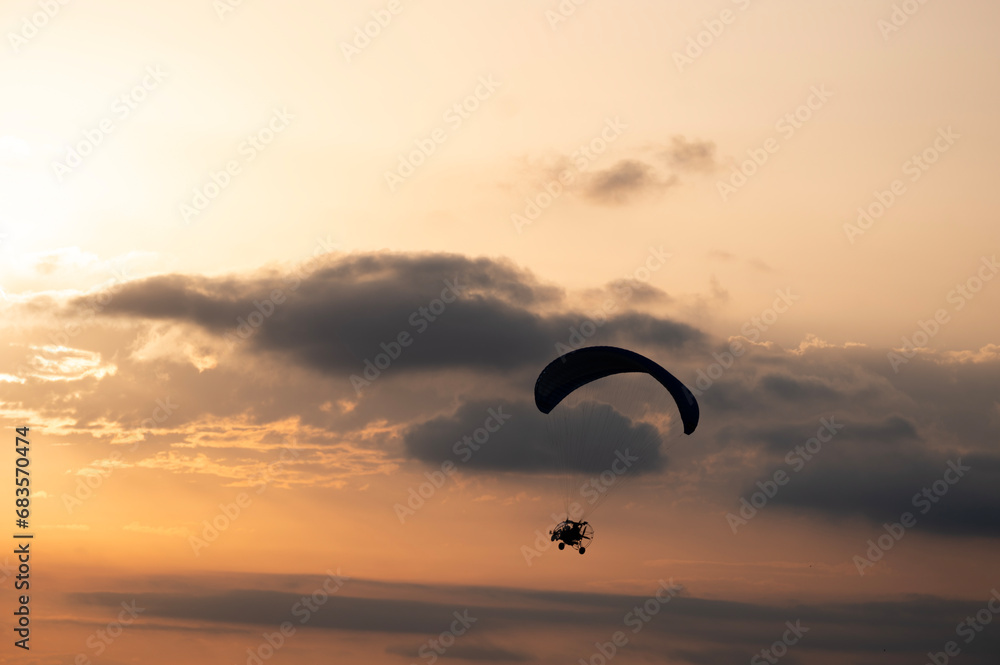 Paramotor tandem flying silhouette in the golden hours with nice clouds on a summer evening