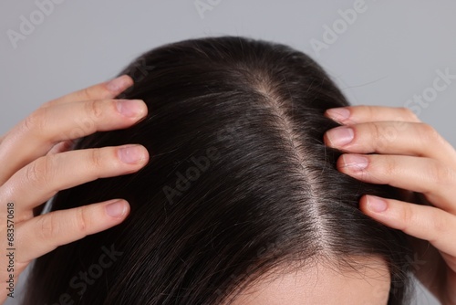 Woman examining her hair and scalp on grey background, closeup