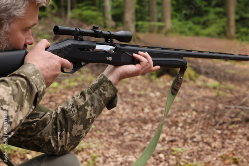 Man wearing camouflage and aiming with hunting rifle in forest, closeup