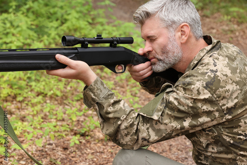 Man wearing camouflage and aiming with hunting rifle in forest