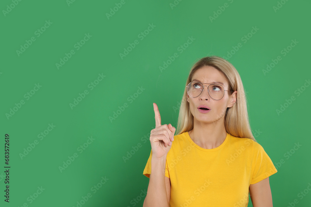 Happy woman in glasses pointing at something on green background. Space for text Happy woman in glasses pointing at something on green background. Space for text