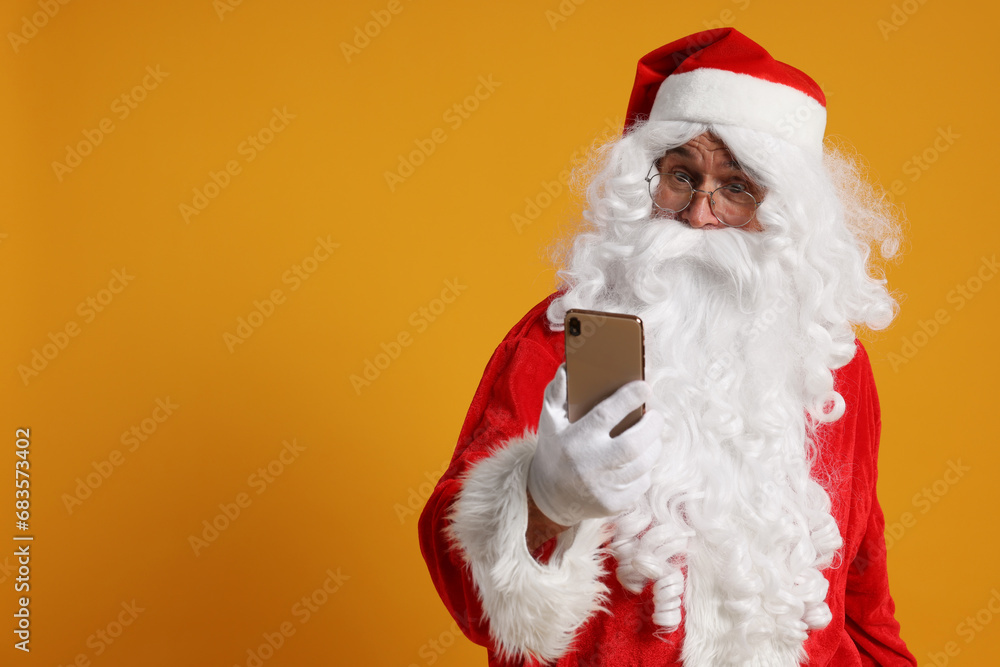 Merry Christmas. Santa Claus using smartphone on orange background, space for text