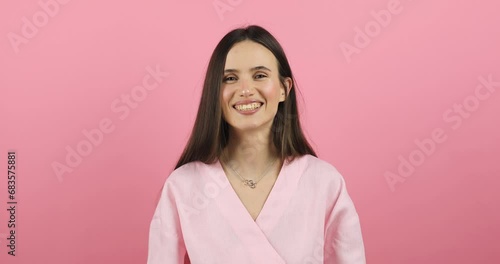 Portrait of young sexy playful brunette girl dressed in pink dress standing isolated over pink background blowing bubblegum candy bubbles and chewing gum. Woman looking at camera, laugh. Slow motion. photo