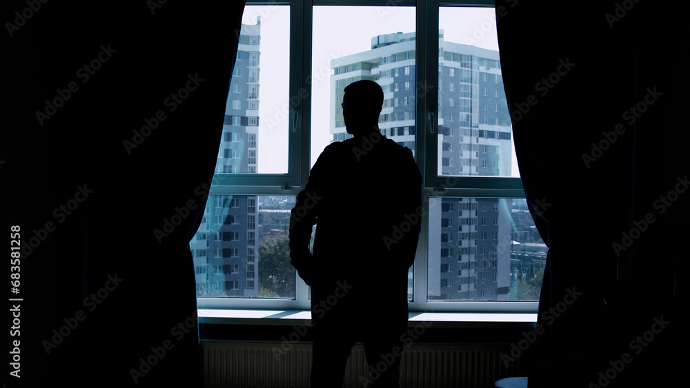 Fototapeta premium Silhouette of a business man talking on a mobile phone on the background of a window and city. Media. Successful confident businessman standing at home by the window.