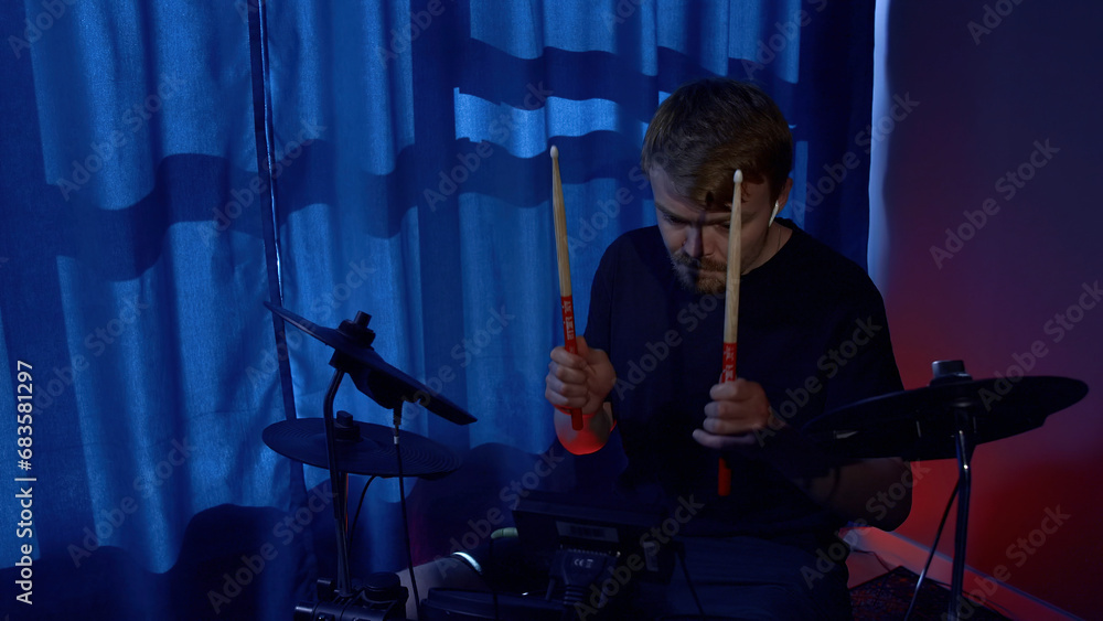 Fototapeta premium Young musician drummer playing drums with drumsticks at sound studio. Media. Man drumming with sticks during rehearsal.