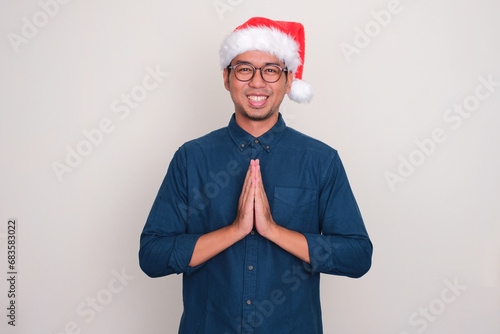 A man wearing christmas hat doing greeting gesture with happy expression photo