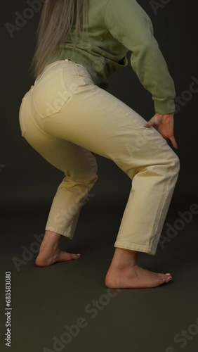 Cropped rear view of woman dancing booty twerking, training dance illuminated changing multicolored club light. Low section of barefoot woman wearing casual clothing - jeans and hoodie. Vertical video