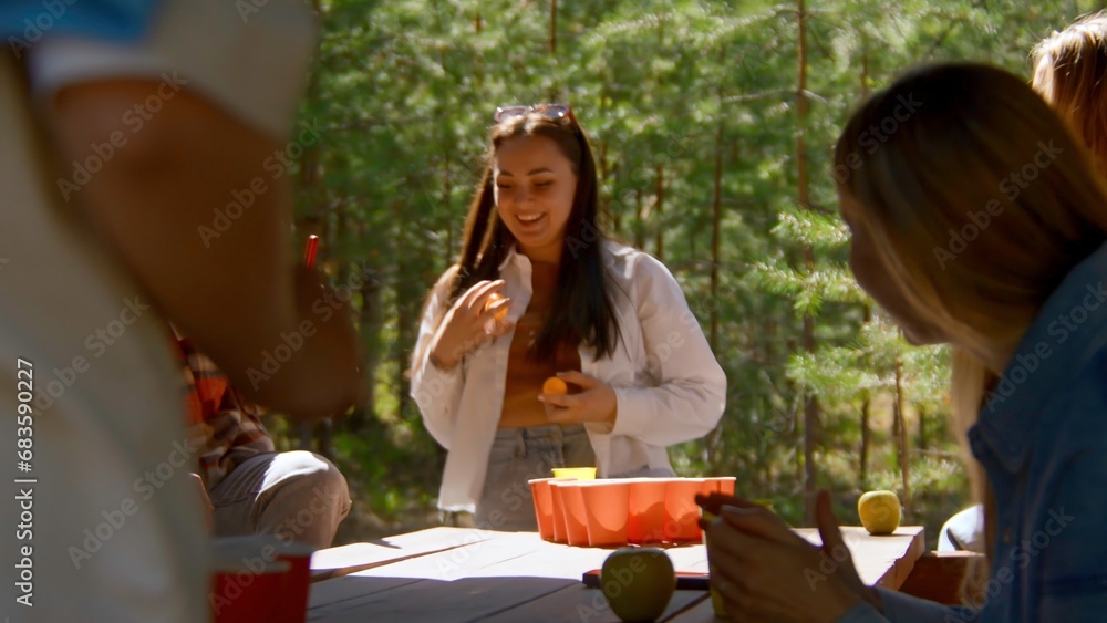 Young people play beer pong. Stock footage. Game for group of friends with glasses of alcohol and ping pong ball. Friends play beer pong in nature in summer