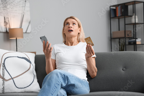 Fotografie Emotional woman with credit card and smartphone on sofa at home