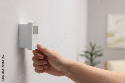Woman adjusting thermostat on white wall indoors, closeup. Smart home system