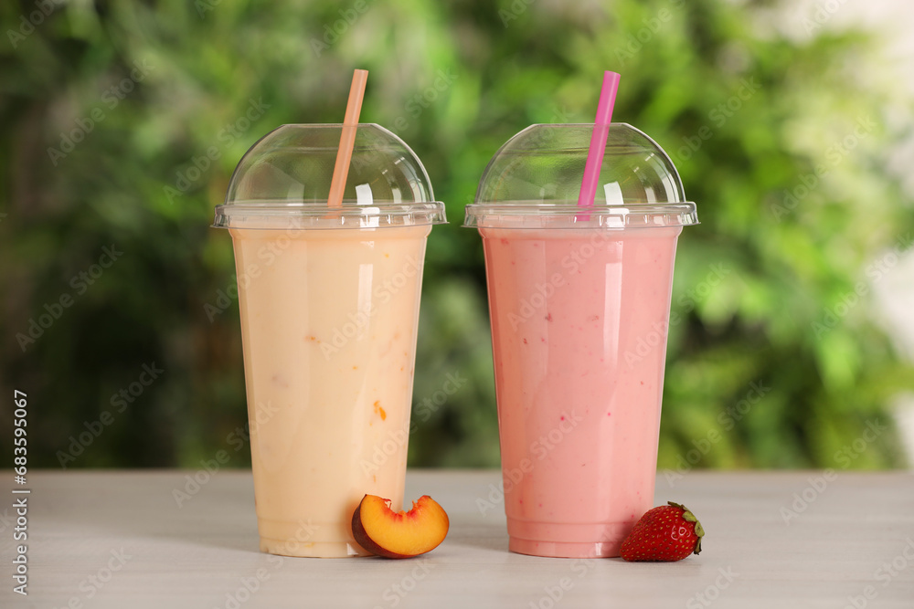 Plastic cups with different tasty smoothies and fresh fruits on wooden table outdoors Plastic cups with different tasty smoothies and fresh fruits on wooden table outdoors