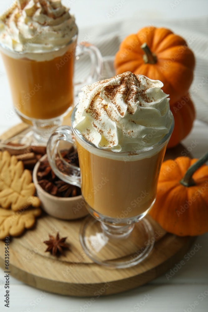 Tasty pumpkin latte with whipped cream in glasses, spices and cookies on white table, closeup Tasty pumpkin latte with whipped cream in glasses, spices and cookies on white table, closeup