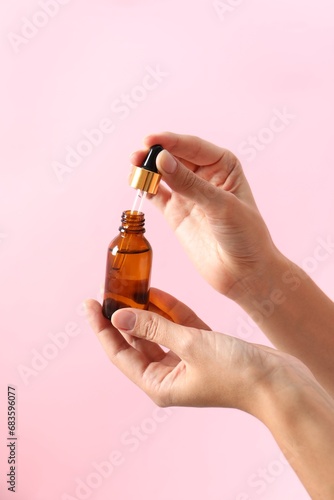Woman with bottle of cosmetic serum and dropper on pink background, closeup