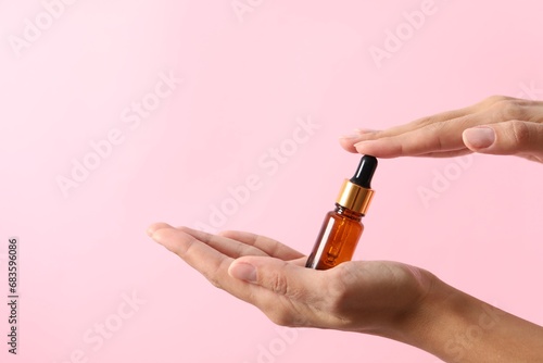 Woman with bottle of cosmetic serum on pink background  closeup. Space for text