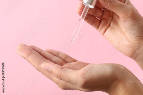 Woman applying cosmetic serum onto her hand on pink background  closeup