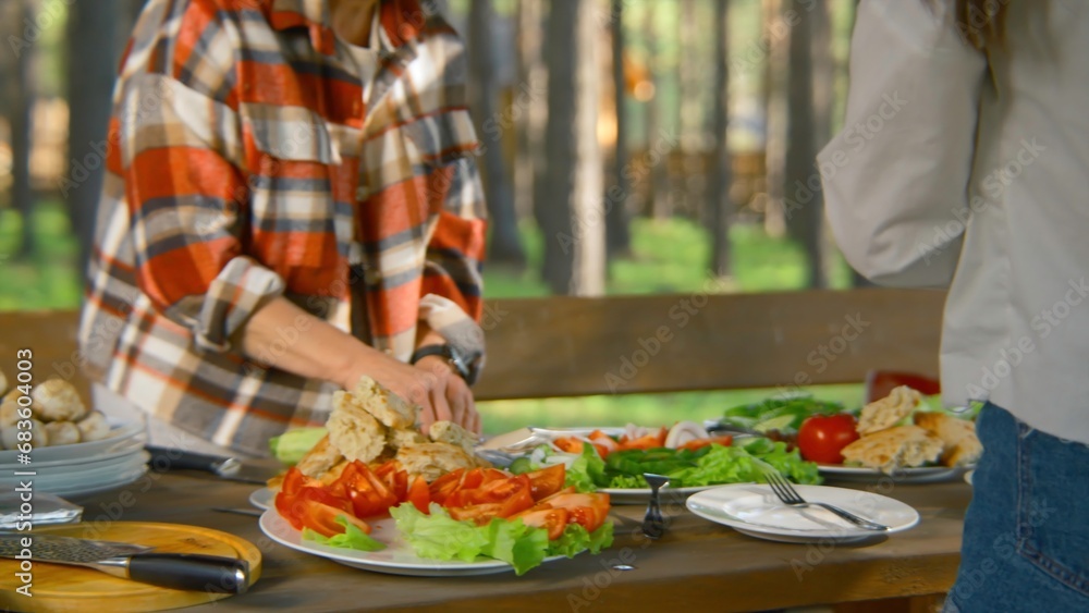 Close-up of people cutting and preparing table in nature. Stock footage. People relax in nature with appetizing table with vegetables. Bright table with vegetables and barbecue in nature