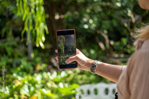 Woman's hand holding a mobile phone taking pictures of a botanical garden