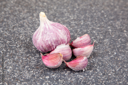 Five cloves and one head of purple garlic together on a cutting board