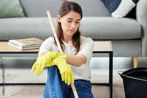 Cleaning, burnout and an unhappy woman in the living room of her home for housework chores. Sad, tired or exhausted with a young person looking bored in her apartment for housekeeping responsibility photo