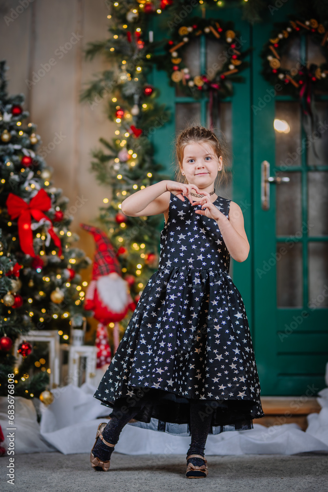 A little girl in a black dress with stars in a Christmas atmosphere. The girl is happy for Christmas. Christmas decorations.