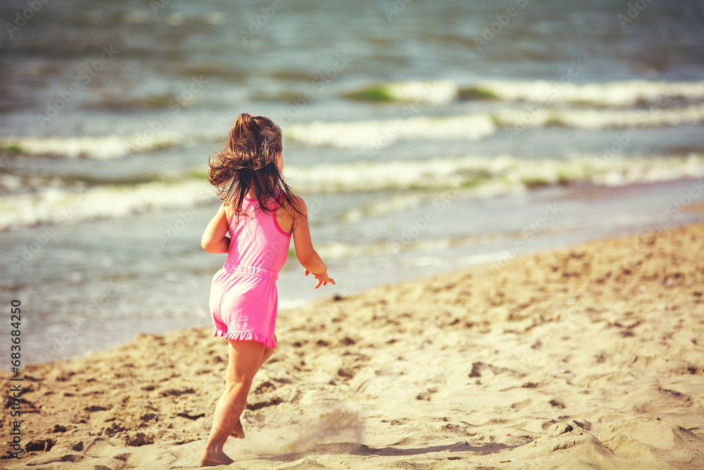 A happy little girl runs on the beach in summer back to the camera