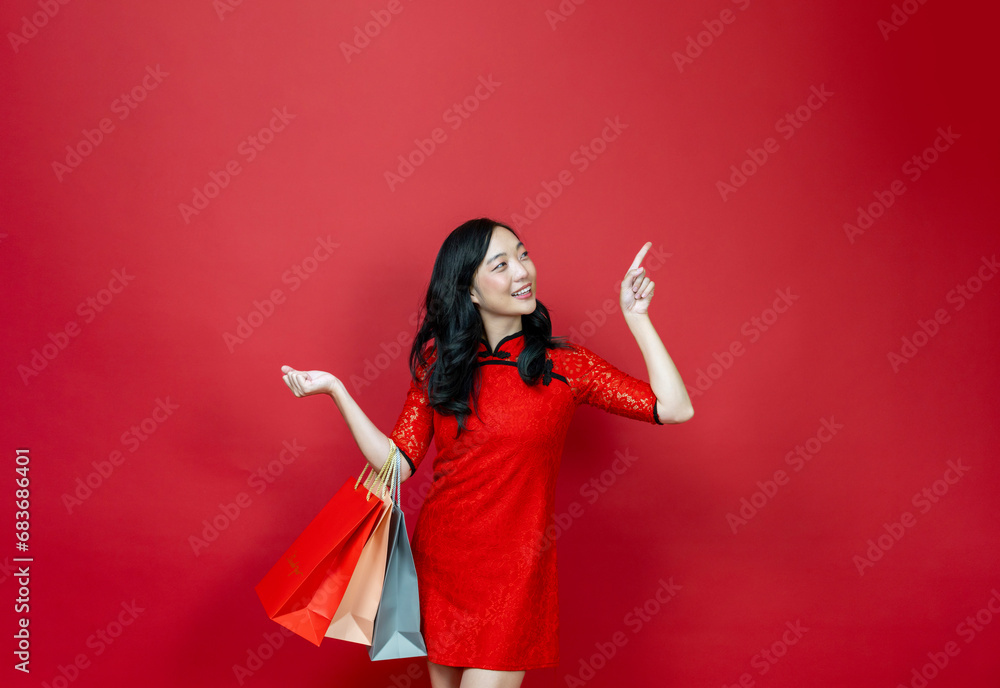 Asian chinese woman with red cheongsam or qipao holding shopping bag wish the good luck sale and prosperity in Chinese New Year celebration holiday isolated on red background Asian chinese woman with red cheongsam or qipao holding shopping bag wish the good luck sale and prosperity in Chinese New Year celebration holiday isolated on red background