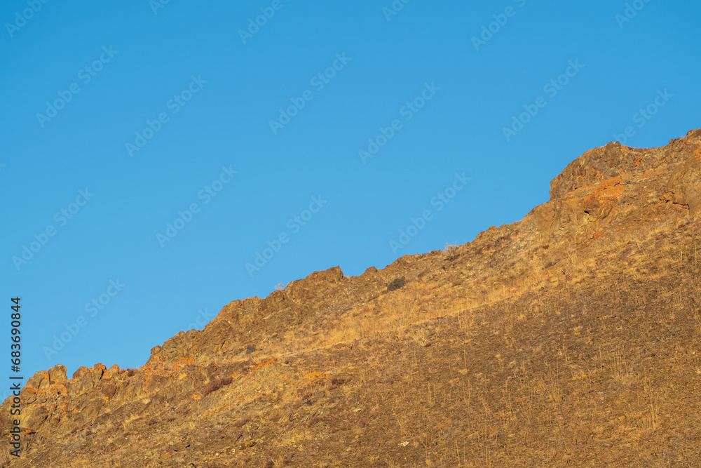 Diagonal red mountain slope against a clear blue sky. View of mountain top and clear blue sky. Diagonal red mountain slope against a clear blue sky. View of mountain top and clear blue sky.