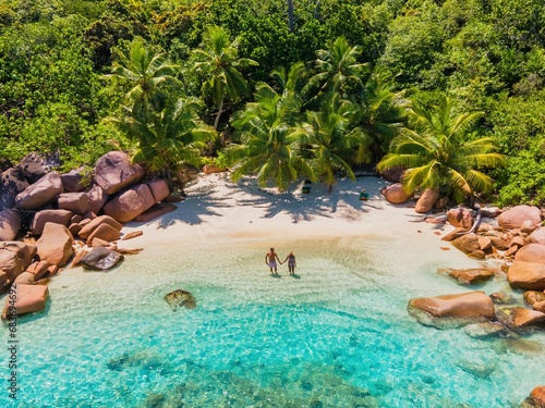  a couple of men and women on vacation at Seychelles visiting the tropical beach of Anse Lazio Praslin Seychelles. Men and women at the beach with crystal clear turquoise colored ocean and palm trees