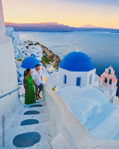 Couple watching the sunset on vacation in Santorini Greece, men and women watching the village with white churches and blue domes in Greece during summer holiday in Greece