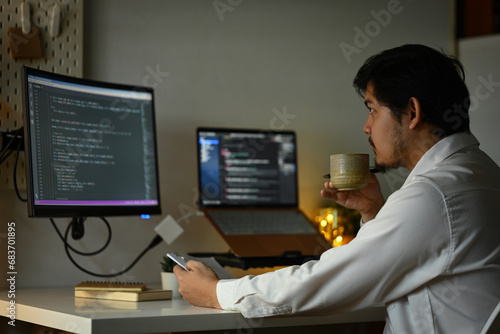 Bearded male software developer drinking coffee and coding at home office