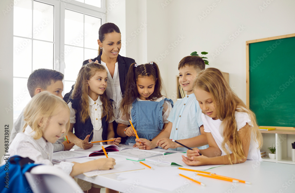 Group of elementary students learning new things in class. Happy children and teacher gather around table in classroom, write in notebooks, draw pictures, and discuss stories. Back to school concept Group of elementary students learning new things in class. Happy children and teacher gather around table in classroom, write in notebooks, draw pictures, and discuss stories. Back to school concept