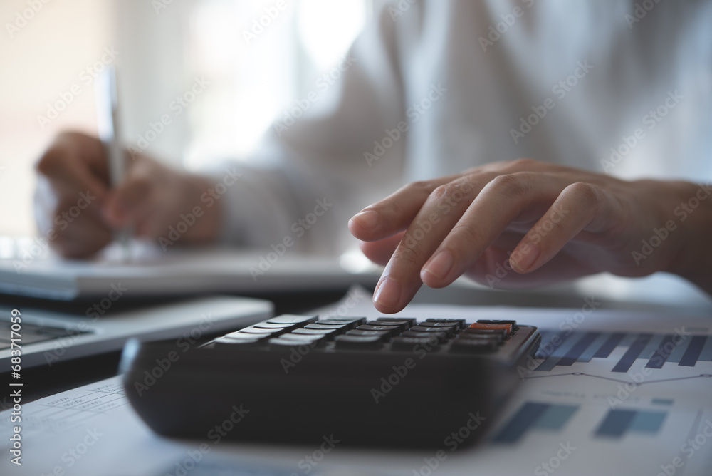 Businesswoman working at office, using calculator to calculate financial report, sales data, with laptop computer and business document on office table, close up. Businesswoman working at office, using calculator to calculate financial report, sales data, with laptop computer and business document on office table, close up.