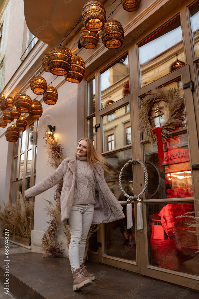 Fototapeta premium Happy young woman in fur coat amidst the festive atmosphere of Christmas on the city street. Christmas mood. Holiday weekend