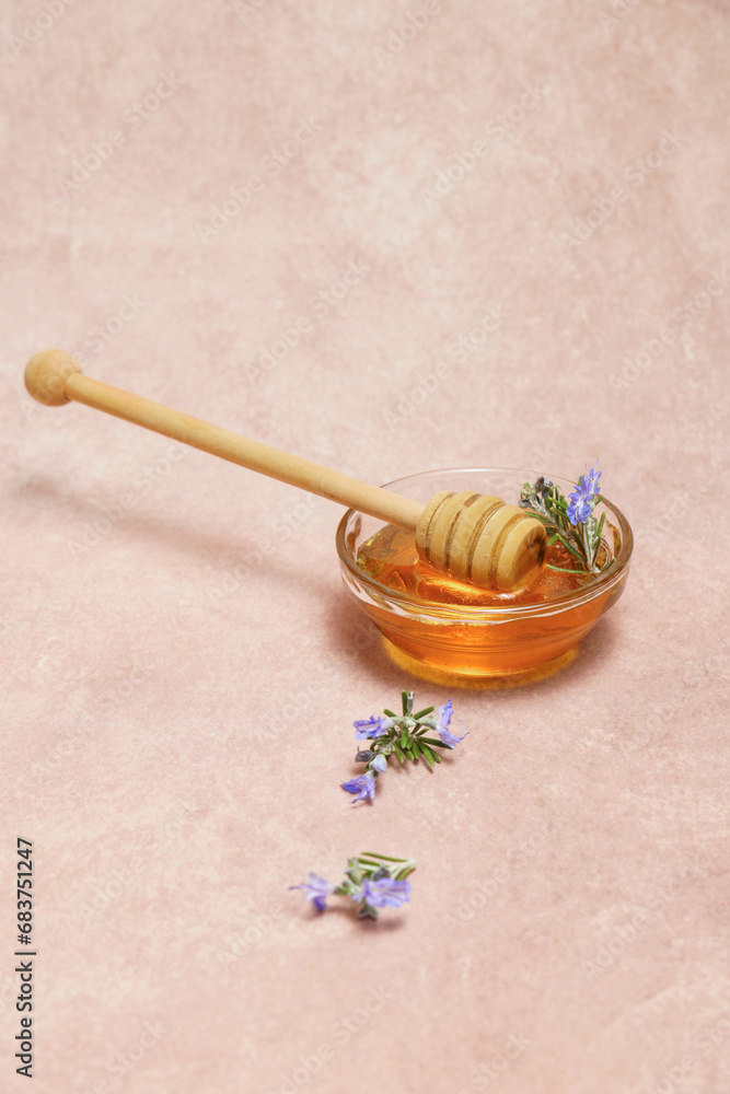 Fototapeta premium natural honey in a glass bowl with a wooden spoon and fresh rosemary sprigs in bloom