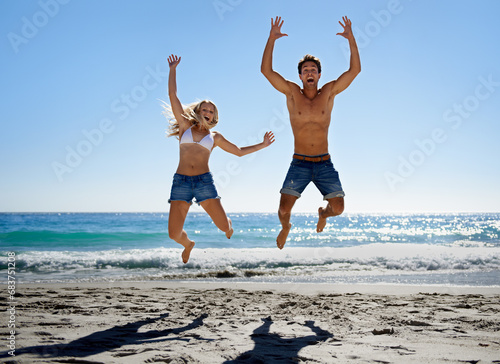 Couple, jump and excited at beach, smile and portrait in summer sunshine for vacation, outdoor or travel. Man, woman and happy with love, bonding and holiday by ocean for adventure in Naples, Italy