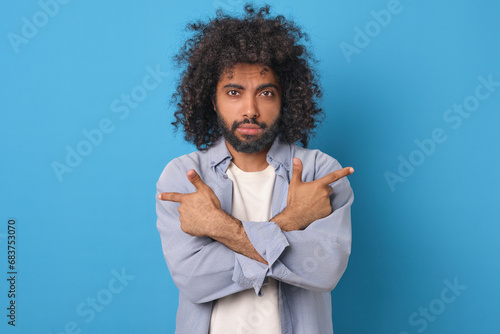Young handsome casual Arabian man points with index fingers of both hands in different directions recommending that you pay attention to advertised product stands posing in blue studio. photo