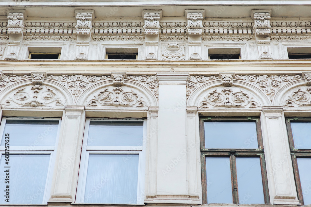 Four large old windows with wooden frames and ornamental reliefs on the wall. Neoclassical building, facade of an old house in Lviv, Ukraine.