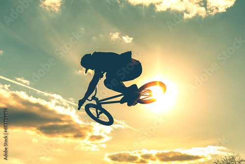 Man on bmx bike against sunshine sky. High BMX jump. Biker silhouette doing an jump.