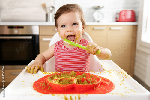 Funny happy baby in high chair eating pea puree with spoon
