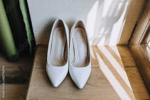 Women's, white leather shoes stand on the parquet close-up. Wedding shoe photography.