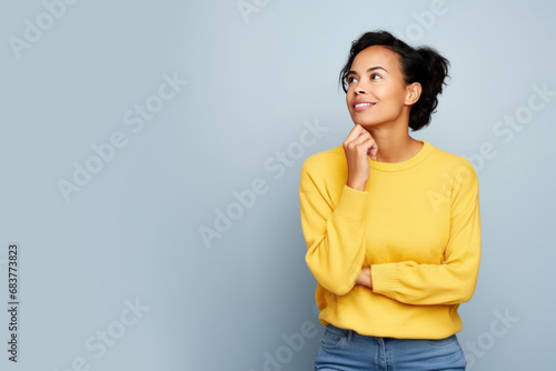 Jeune femme en train de penser en regardant sur le côté vers le haut, espace libre pour du texte ou mise en scène, tenue jaune fond uni gris pâle