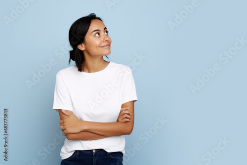 Jeune femme en train de penser en regardant sur le côté vers le haut, espace libre pour du texte ou mise en scène, tenue claire fond uni bleu pâle photo