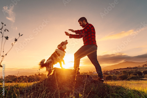 Young man standing in the field playing and training with his border collie breed dog at sunset. life with pets photo