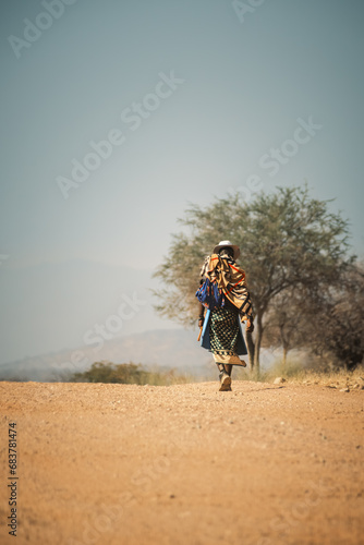Local man in traditional attire walking on roadside of highway C43 near Epupa Falls, Kunene Region, Namibia.