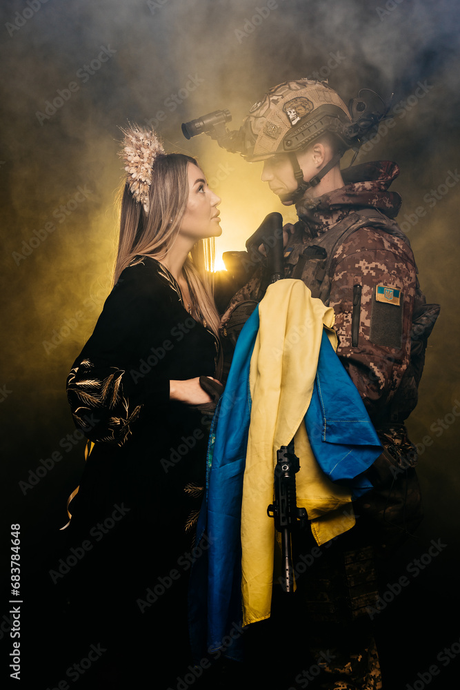 Obraz premium A couple in love at dawn during a battle in the smoke holds the flag of Ukraine in their hands. The concept of invincible love, the victory of Ukraine over the Russian invasion.