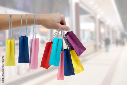 Crop female hand holding colorful paper bags on background of shopping center. black Friday