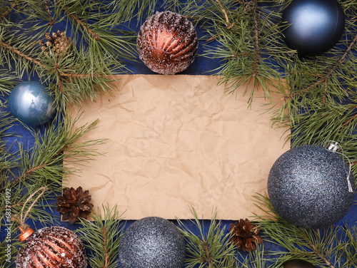 Crumpled sheet of craft paper with copy space for Christmas text, blue ball, glittering brown baubles, natural fir branches, New Year festive decoration. Xmas creative greeting template