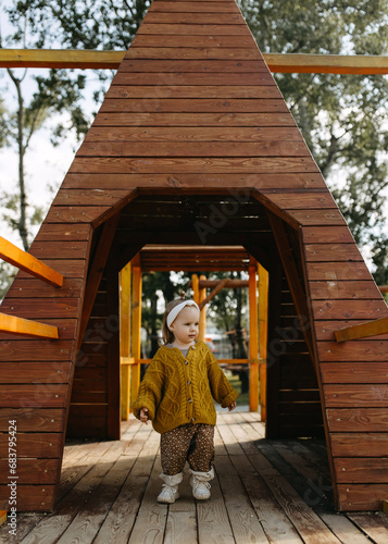 Child playing at a big wooden playground, standing under a wooden tent.