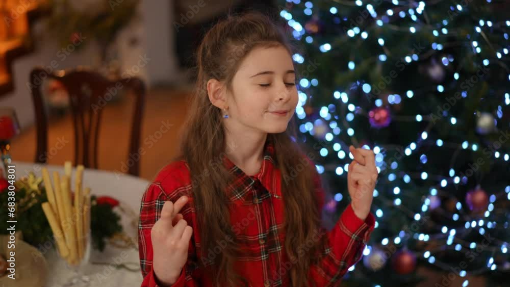 Slow motion. In the living room, near the Christmas tree, a girl, closing her eyes and crossing her fingers for good luck, makes wishes Slow motion. In the living room, near the Christmas tree, a girl, closing her eyes and crossing her fingers for good luck, makes wishes