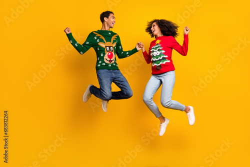 Full length photo of two overjoyed ecstatic people hold hands jump raise fists christmas magic isolated on yellow color background